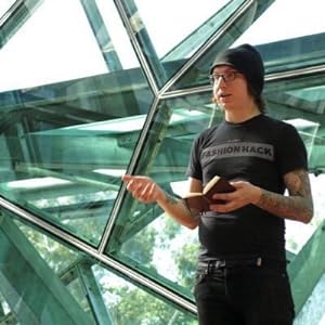 Man in black t-shirt and beanie in front of glass panels.