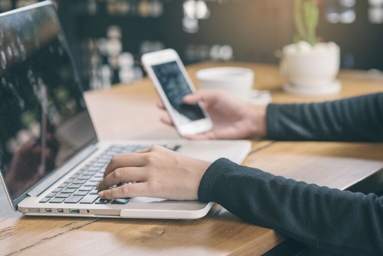 Businesswoman on laptop and phone researches a company on social media