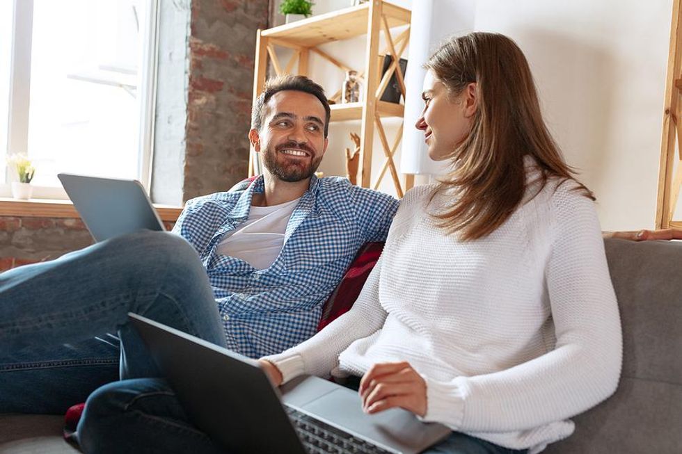 A couple sits together as they update their LinkedIn profiles on their laptops