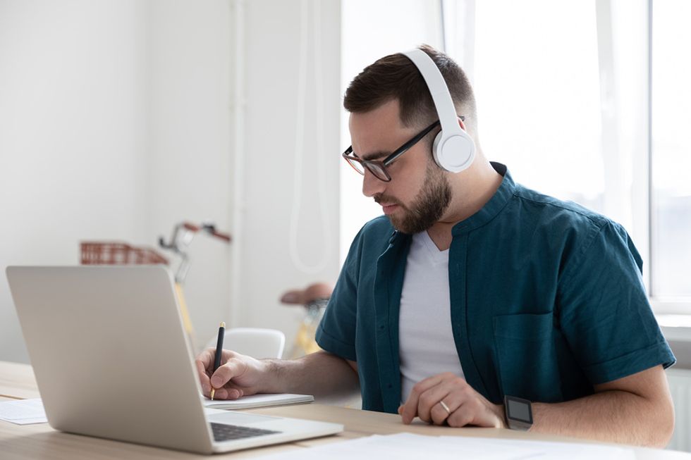 Man on laptop listening to music writes down is career growth plan