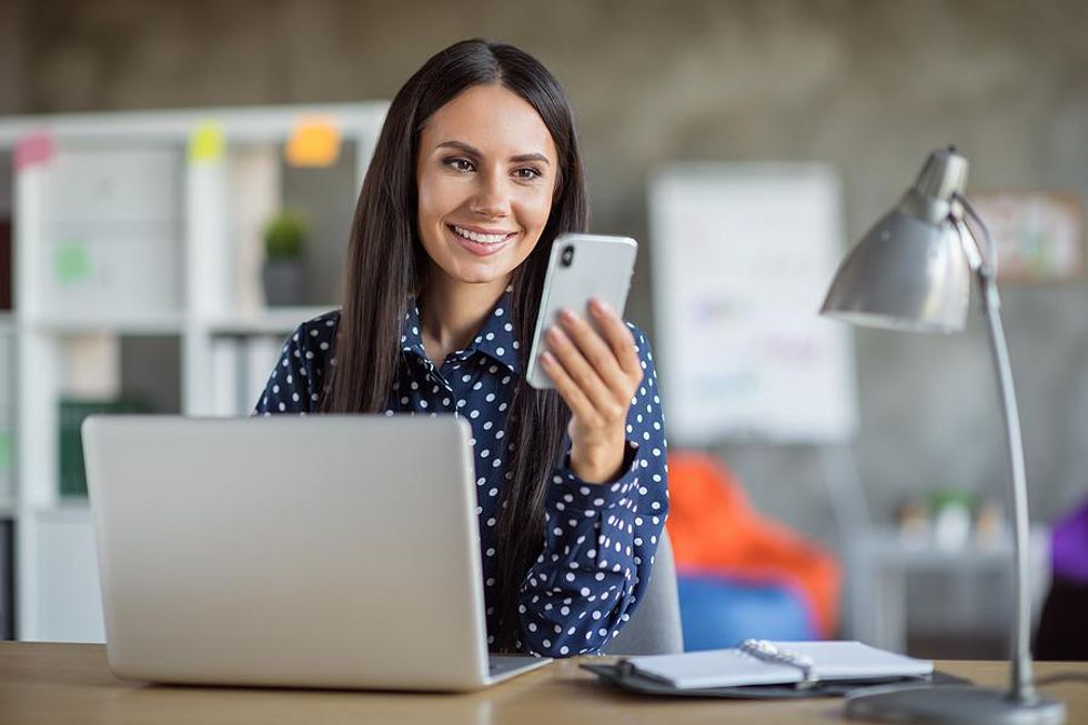 Woman on phone and laptop posts content on LinkedIn aligned with her personal brand